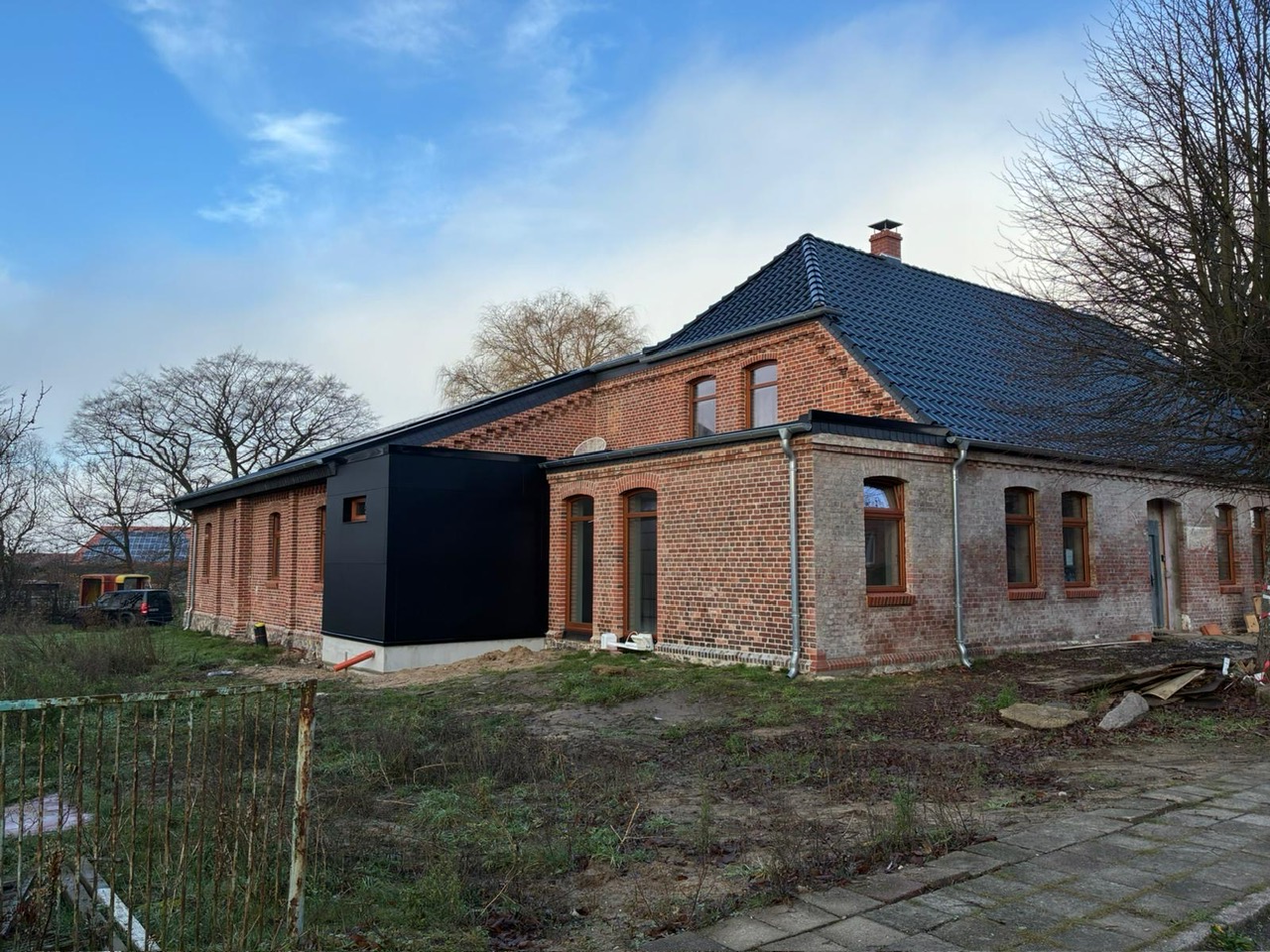 Backsteingebäude mit neuem dunklen Ziegeldach und schwarzem Anbau